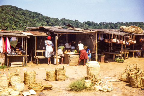 Woman at local market selling fruit and handicrafts including baskets.
