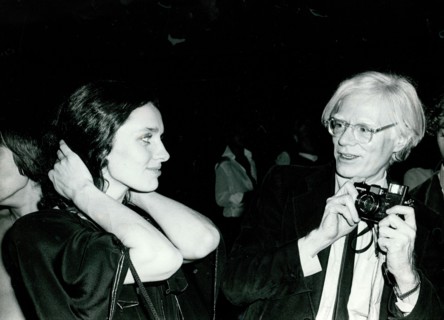Andy Warhol holds a camera as Margaret Trudeau pulls back her hair