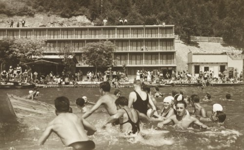 Italy, Trieste, group of people enjoying the sea,  three-story rationalist building in the background is the former Bagno Excelsior of Barcola, 1940 circa