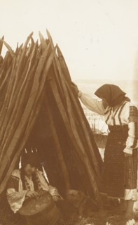 Two women in traditional Romanian clothes under a hut
