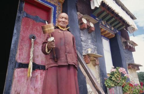 CHINA, Tibet, Samye Monastery, Lama holding prayer wheel outside monastery door.