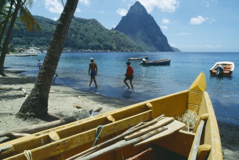 WEST INDIES, St Lucia , Soufriere, People walking along beach with boats moored offshore and the