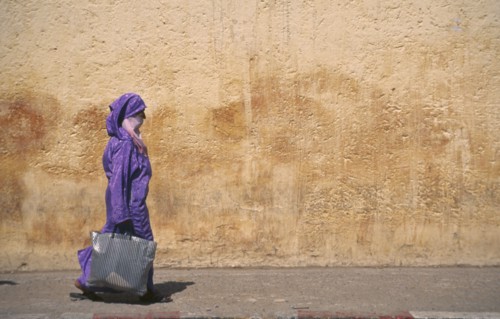 MOROCCO, Traditional Clothing, Woman with veil waliking past colourful wall.