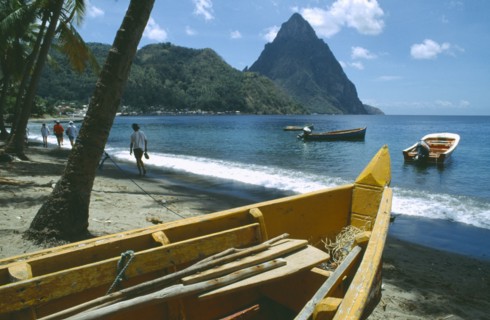 WEST INDIES, St Lucia, Soufriere, People walking past fishing boats on beach with the Pitons in the