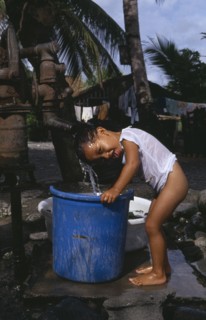PHILIPPINES, Mindoro, Roxas, Young boy taking shower under water pump .