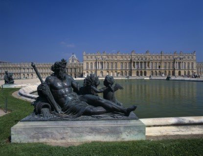 FRANCE, Ile de France, Versailles, Bronze statue beside lake with palace behind and clear blue sky