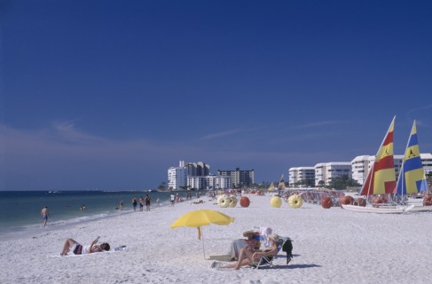 USA, Florida, St.Petersburg, Woman reading under a multicoloured parasol on a sandy beach with