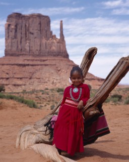 USA, Arizona, Monument Valley, Navejo girl leaning against dead tree wearing a red dress and