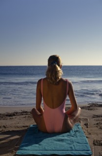 USA, Florida, Sunbathing, Young woman on sandy beach sitting in a meditation position on a green