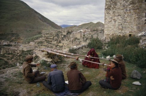 CHINA, Tibet, Ganden, Men blowing long horns on a hillside at Ganden Monastery