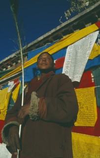 TIBET, Lhasa, Jokhang Temple, Male pilgrim standing outside temple in front of prayer flags