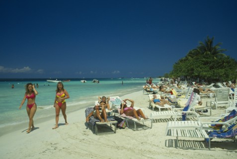 WEST INDIES, Jamaica, Negril, Female tourists beach sunbahing on sun loungers by the water with two