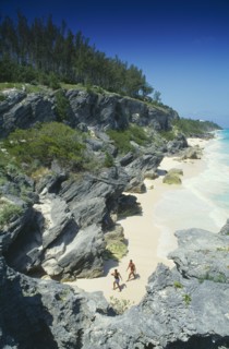 BERMUDA, Astwood Park, Couple walking on beach towards rocky cliffs