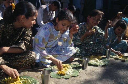 INDIA, Himachal Pradesh, Kulu, Girls eating from banana leaves with their hands at meal during