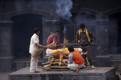 NEPAL, Kathmandu, Cremation at Pashupatinath Temple.  Men gathered to light funeral pyre.