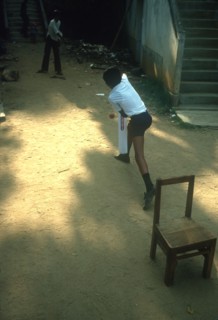 SRI LANKA, Kandy, Young boys playing Cricket in street using a wooden chair as stumps
