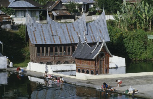 INDONESIA, Sumatra, Minankabu house with people washing clothes in the lake outside