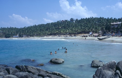 INDIA, Kerala, Kovalam, View from rocky outcrop over bay toward beach surrounded by palms with