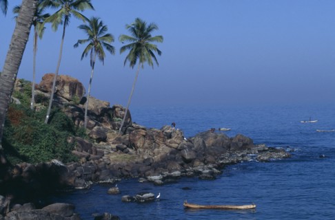 INDIA, Kerala, Kovalam, Coastal scene with coconut palms on rocky promontory and men in boats