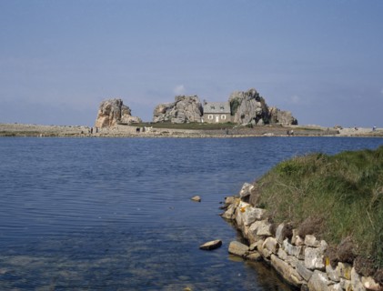 FRANCE, Brittany , Plougrescant, Overlooking an expanse of water to a house surrounded by rocks.