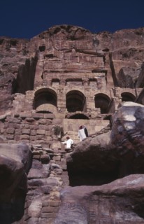 JORDAN, Petra, View looking up at historical tombs carved in sandstone cliffs with two men dressed