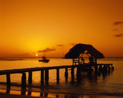 WEST INDIES, Tobago, Pigeon Point, Wooden jet and boat silhouetted at sunset.