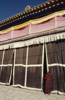 CHINA, Quinghai, Tongren, Monk standing at the entrance to a Tibetan monastery