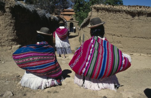 BOLIVIA, Lake Titicaca, Isla del Sol, Yumani Villagers carrying brightly coloured bundles over