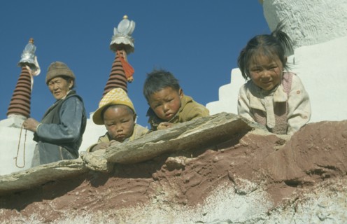 CHINA , Tibet , Catsall , Three children looking down over wall with elderly woman standing behind.