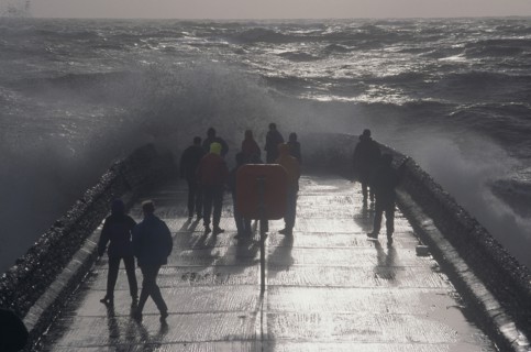 ENGLAND, East Sussex, Brighton, Waves crashing over a groyne with people on it