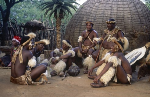 SOUTH AFRICA, KwaZulu Natal, Tribesmen sitting on the ground outside a hut whilst the chief sits on