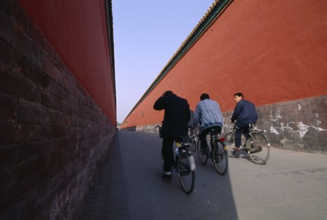 CHINA, Hebei, Beijing, Imperial Palace with cyclists riding down a long red alleyway