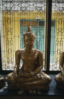 THAILAND, Bangkok, Seated Buddha covered with gold leaf in front of window with decorative metal