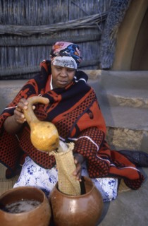 SOUTH AFRICA, Qwa Qwa, Basotho Cultural Village, Basotho woman pouring beer into a strainer from a