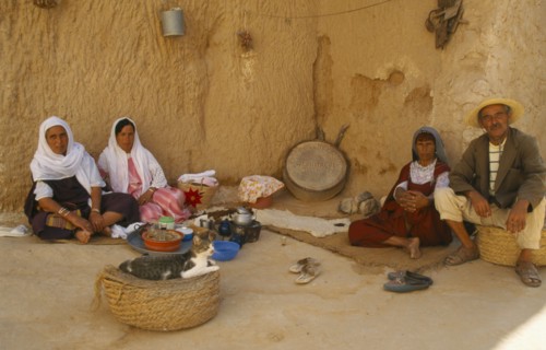 TUNISIA, Matmatah, Troglodyte Cave with men and women sitting by the wall with a cat in a basket in