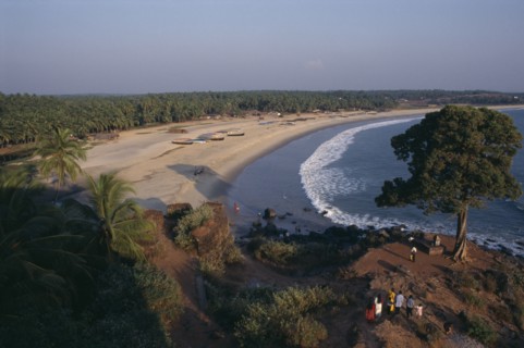 INDIA, Kerala, Bekal, View along the beach and coastline with people standing by tree on rocky