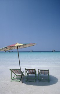 THAILAND, Pattaya , Coral Island, Empty sun loungers and umbrella on beach with boats moored just