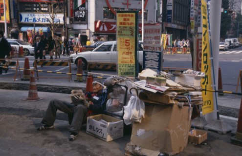 JAPAN, Honshu, Tokyo, Homeless man living on the street with his cardboard home at a busy road