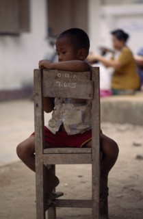 THAILAND, North, Mae Sai , Karen refugee boy sitting on chair