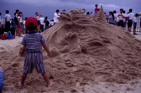 SINGAPORE, Beach, Sand sculpture of a Dragon with a boy standing in front of it holding a handful