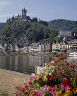 GERMANY, Rhineland, Cochem, Hilltop castle overlooking houses beside the Mosel River with flowers