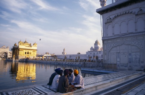 INDIA, Punjab, Amritsar , Group of Sikh men sitting on marble walkway surrounding sacred pool