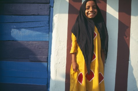 INDIA, Kerala , Kochin, Muslim girl standing in front of building wall painted with red and white