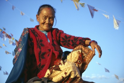 NEPAL , Kathmandu, Bodnath, Smiling female Tibetan refugee sitting amongst prayer flags on roof of