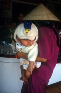 VIETNAM, Tay Ninh, Woman in a straw hat holding a baby as she looks at a shop display in Tay Ninh