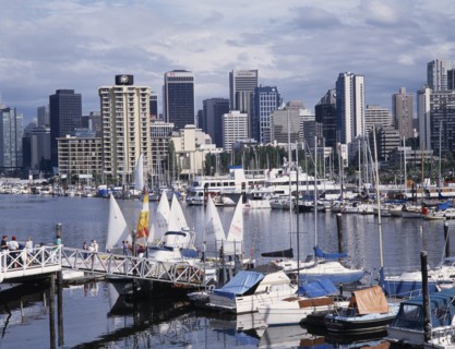 CANADA, British Columbia, Vancouver, City skyline over busy yacht harbour with people walking on