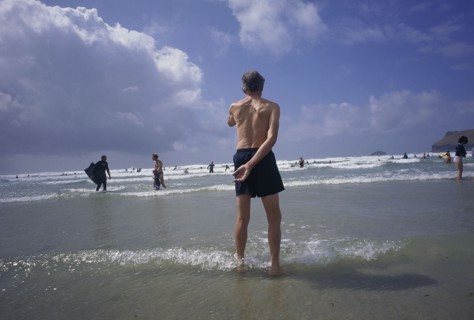 ENGLAND, Cornwall, Polzeath, Man standing in shallow water on the beach looking out to bathers in