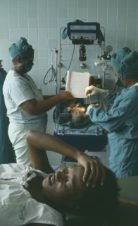 CUBA, Havana, Woman lying with her hand on her head after giving birth while two nurses weigh her