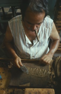 CUBA, Sancti Spiritus, Trinidad, Man smoking a cigar whilst he rolls cigars in a cigar factory