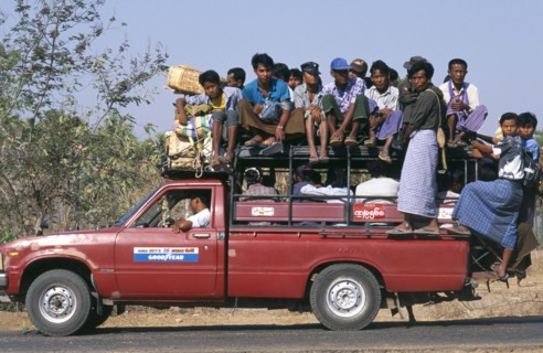 MYANMAR, Bagan, Overcrowded country minibus with people on the roof and hanging of the back  Burma